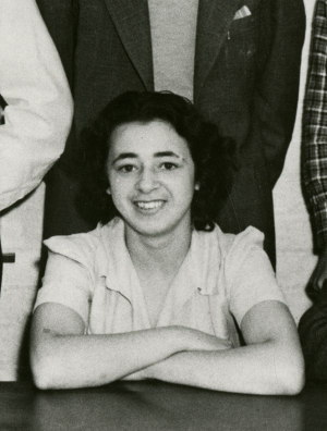 Portrait of a woman, Helen Powell, smiling and sitting at a table with her arms crossed