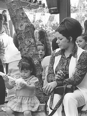 View of Mexican family seated on brick wall; children holding cotton candy; other people in background.