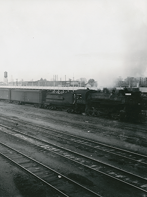 View of Southern Pacific Railroad yard in Sacramento. Locomotive number 2359 is seen along with freight cars. A water tower is seen in the distance.