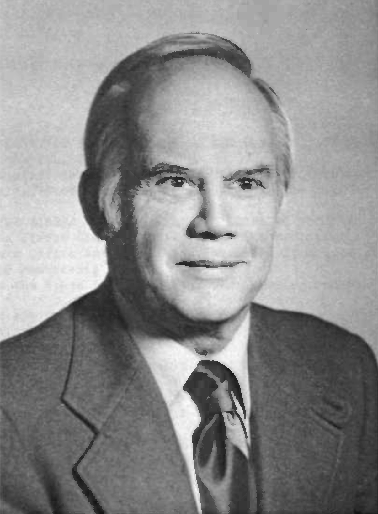 Portrait of John Zierold. In a black and white photograph, an older white man is seen seated, wearing a suit coat, white shirt, and dark tie, looing at the camera.