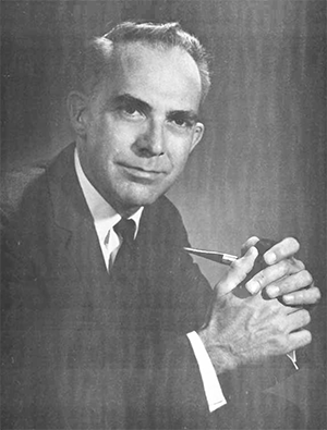 Portrait of William E. Siri. In a black and white photograph, an older white man is seen seated, wearing a dark suit, white shirt, and dark tie, clasping his hands while holding a pipe, looing at the camera.